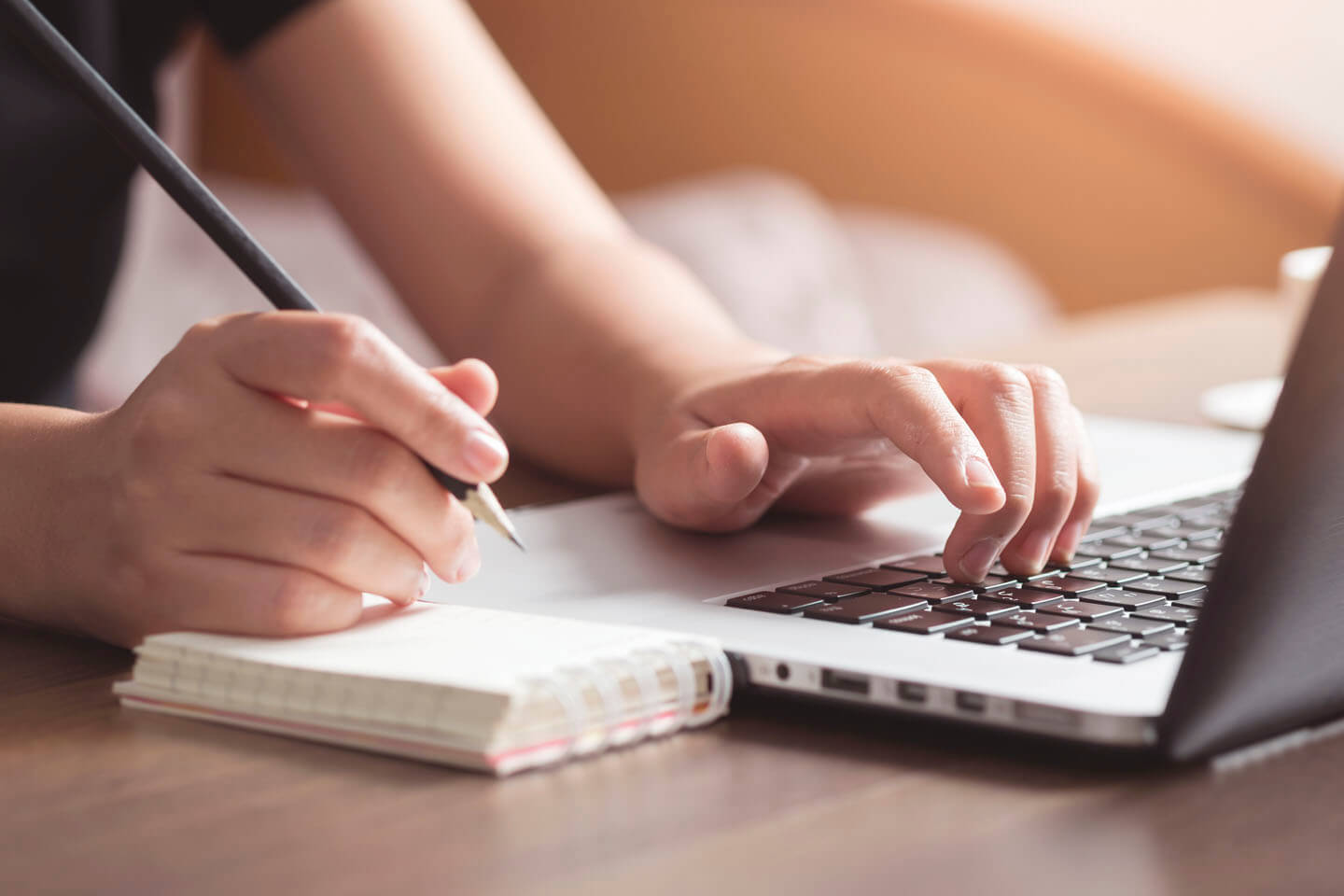 A woman making notes whilst working on a laptop