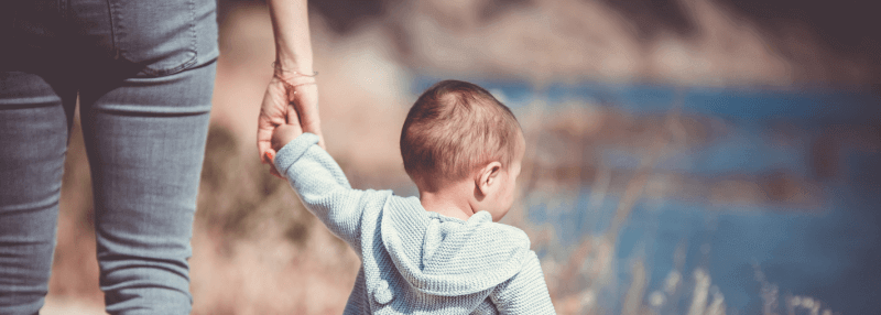 young child holding the hand of an adult but a lake