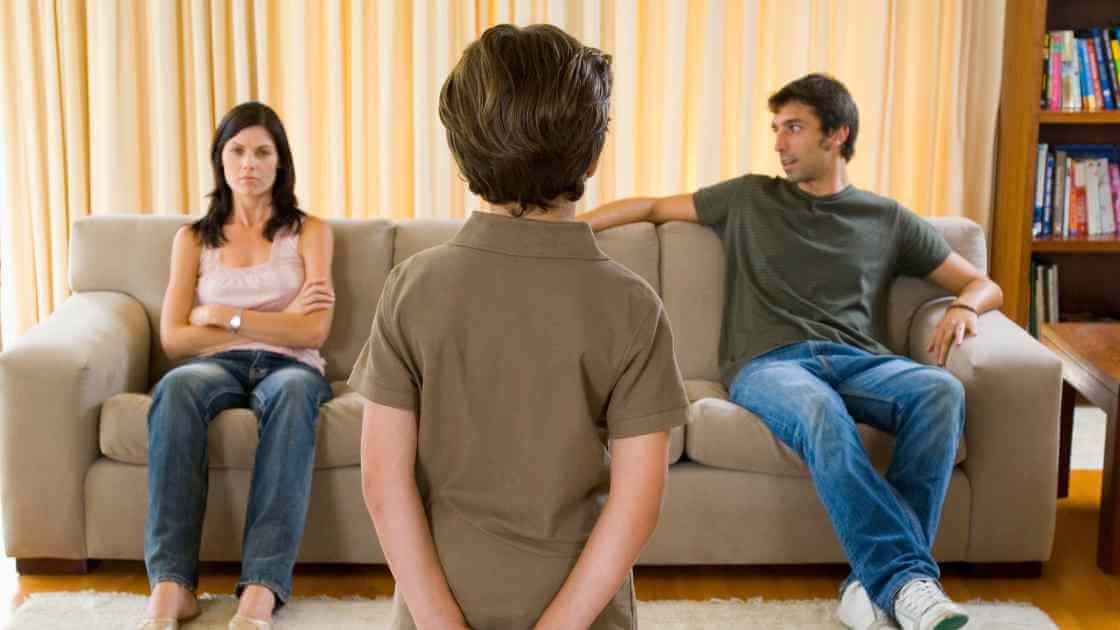 Parents sit on sofa looking unhappy with child in the foreground